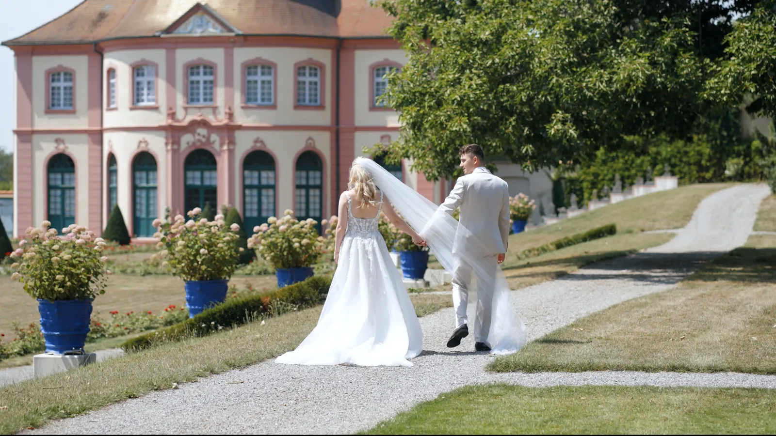 Brautpaar mit wehendem Schleier auf dem Weg zum Barockschloss, Titelbild des Hochzeitsfilms von Simea und Basil
