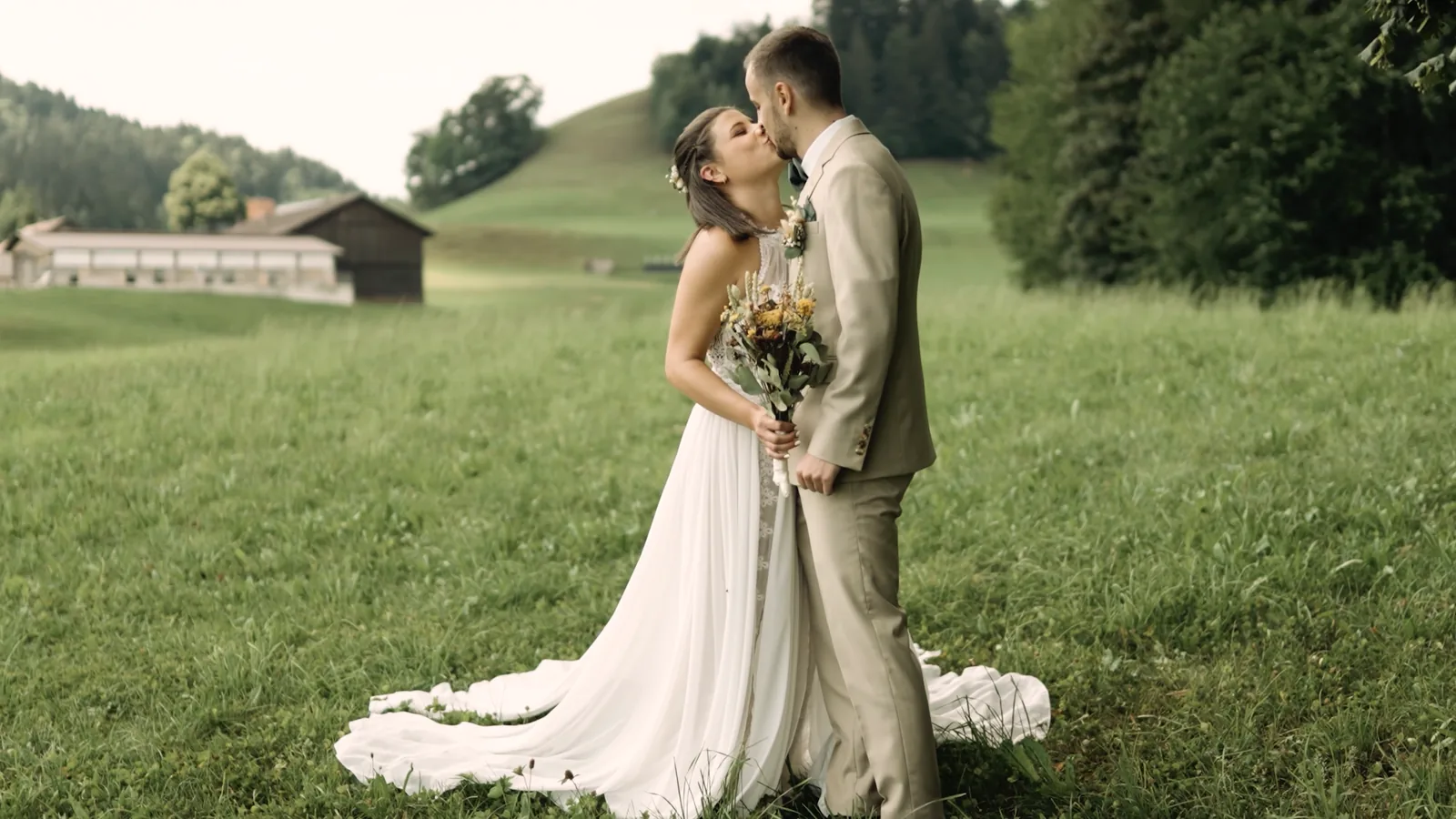 Hochzeitstrailer von Raphael Cyrill Films: Kuss des Brautpaares auf einer Wiese vor den Hügeln des Zürcher Oberlands